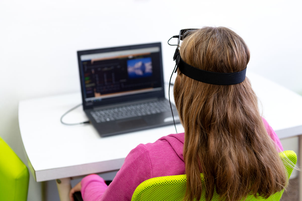 Femme avec un casque neurofeedback assise devant un ordinateur.